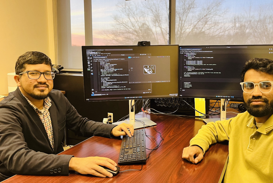 Two guys talking with a computer behind them