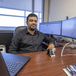 Dr. Alvi Ataur Khalil seated at his office desk with computer monitors and an award behind him.